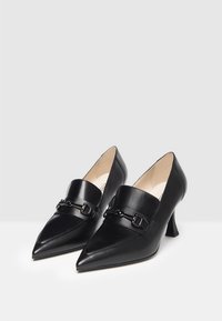 Zwarte leren hoge hakken met spitse neuzen, voorzien van een gladde matte textuur, een decoratieve band met een gesp en een lage blokhak.
