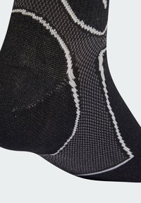 Černá ponožka s текстurovaným vzorem, s bílými akcenty a zesílenou patou. Tkanina vypadá elasticky a prodyšně.