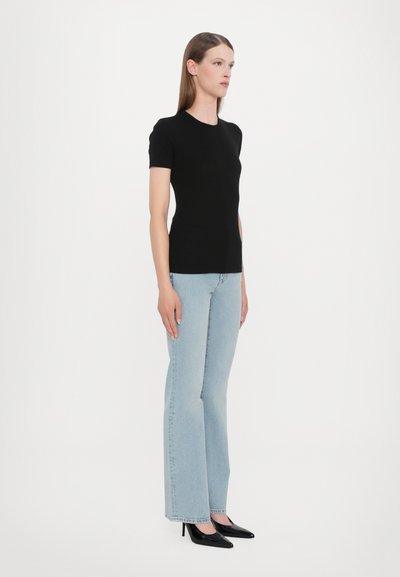 Black short-sleeve fitted T-shirt, crepe texture, paired with light blue flared jeans and black pointed-toe heels. Minimalist design, solid colors.
