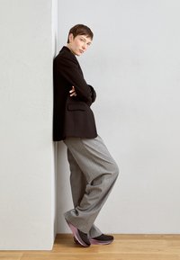 Black tailored blazer over a white shirt, paired with light gray pinstriped trousers and brown and pink shoes against a neutral background.