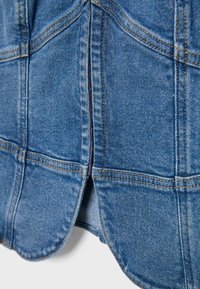 Gros plan sur un tissu en denim bleu avec une double couture visible, des coutures et un détail fendu sur l'ourlet inférieur.