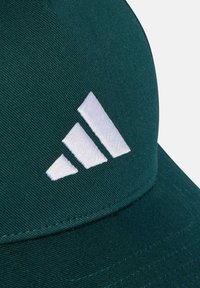 Gorra de béisbol verde hecha de tela texturizada, con un logotipo de Adidas blanco bordado y tres rayas diagonales en la parte frontal.