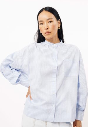 Chemise boutonnée rayée bleu clair avec un col haut, coupe décontractée et poche poitrine. Fabriqué à partir d'un tissu lisse avec une texture plate.