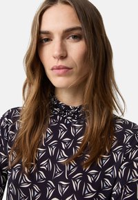 Halenka s dlouhým rukávem a stojatým límcem, vyrobená z námořnické látky zdobené bílým a světle modrým květinovým vzorem. Hladká textura a měkký drap.