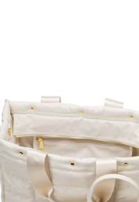 Witte gewatteerde draagtas met gouden hardware, voorzien van een bovenste ritssluiting en een binnenzak. Stevige stoffen handvatten en een gladde textuur.