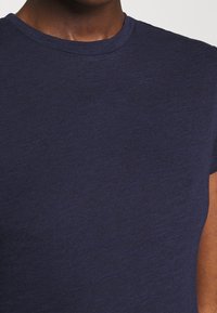 Gros plan d'une personne portant un t-shirt uni bleu marine à col rond, montrant le cou et le haut de la poitrine.