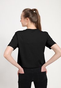 Czarny bawełniany t-shirt z krótkimi rękawami, okrągłym dekoltem i luźnym krojem, noszony z ciemnymi spodniami, prezentujący gładką fakturę.