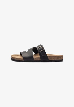 Black leather slide sandals with adjustable strap and buckle, cork footbed, textured rubber outsole, minimalist design.