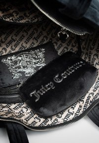 Svart sammetspåse med insida som har ett silverbesmyckat fack och en kontrasterande mönstrad foder med texten "Juicy Couture".