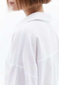 Witte blouse met een gladde textuur. Heeft een klassieke kraag, zichtbare naaddetails en een relaxte fit.
