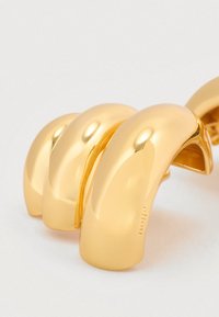 Βραχιόλι από μεταλλικό υλικό με χρυσή απόχρωση, που διαθέτει τρία λείων, στρογγυλεμένων τμημάτων με γυαλιστερό φινίρισμα και διακριτικό χάραγμα στο εσωτερικό μέρος.