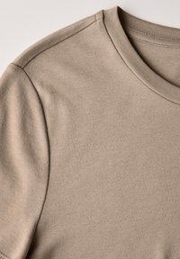 Beige puuvillane T-särk ümmarguse kaelusega, sile tekstuur ja lühikesed varrukad. Kangas on ühtlaselt õmmeldud minimalistliku disainiga.