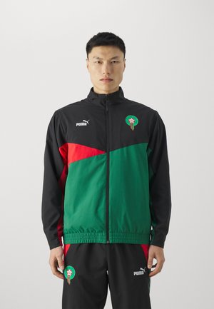 Chaqueta deportiva con un diseño en negro, verde y rojo, que presenta un cierre de cremallera en la parte delantera, cuello alto y el logo de Puma. Incluye un detalle del emblema marroquí.