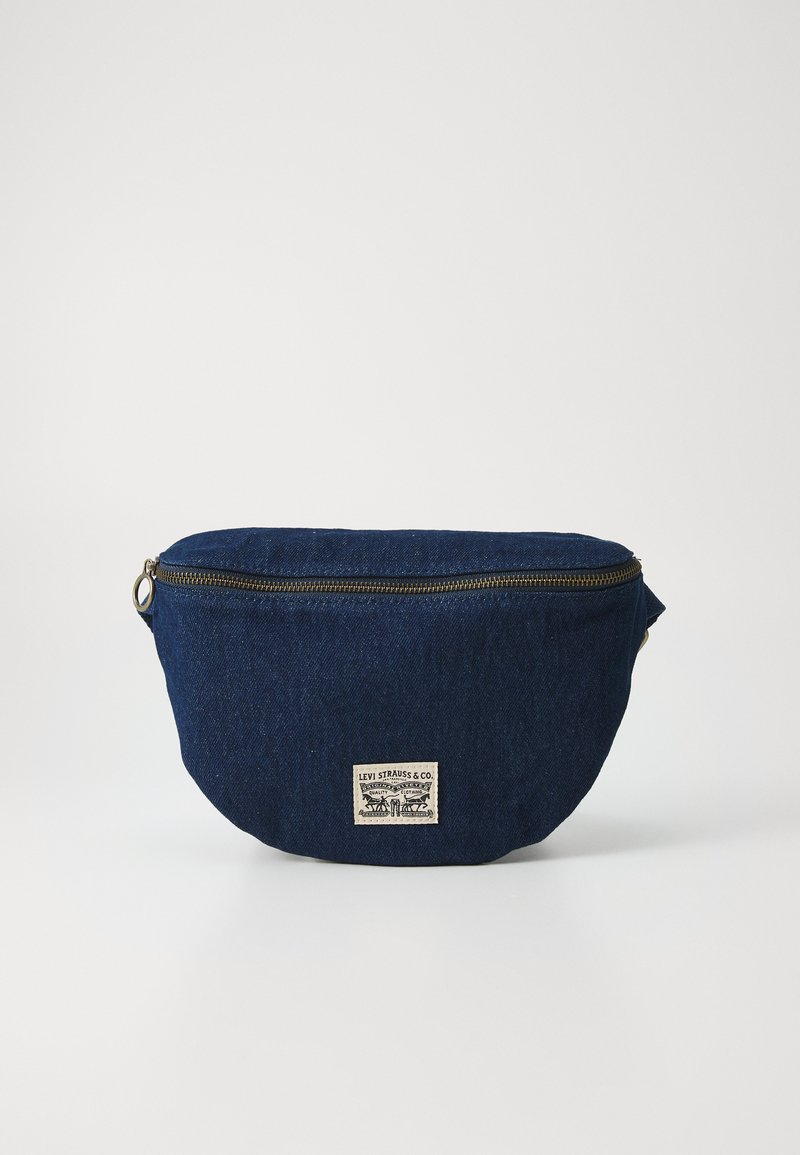 Mornarsko modra denimska torbica za lične stvari z zaobljeno obliko, zlatim zadrgo in bež blagovno znamko na sprednji strani, ki prikazuje vintage logotip.