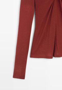 Dlouhý rukáv top v tmavě červené barvě, s hladkou, jemnou texturou a shromážděným designem na přední straně, se rovnými okraji.