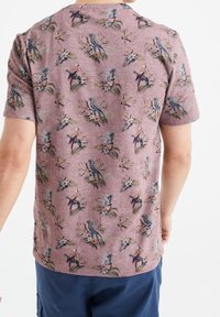 Koszulka z krótkim rękawem w kolorze mauve z wzorem ptaków i kwiatów, o teksturowanym wykończeniu i okrągłym dekolcie.