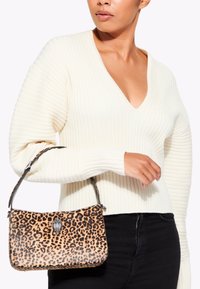 Sac à main en imprimé léopard avec une sangle noire et des détails en métal argenté, présentant une texture lisse. Porté avec un pull à côtes blanc et un jean noir.