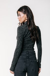 Bluză neagră cu mâneci lungi, fir metalic argintiu, guler înalt și țesătură texturată, asortată cu blugi negri cu talie înaltă.