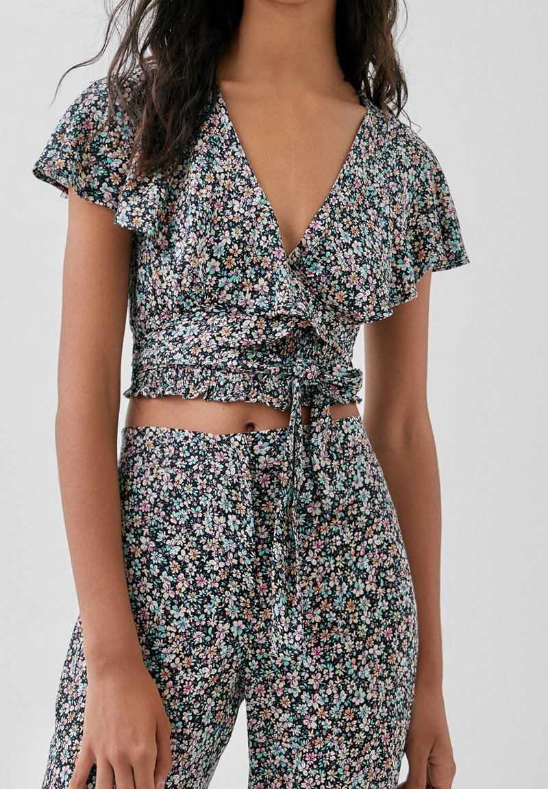 Haut court cache-cœur à fleurs avec fond noir, manches courtes à volants et ourlet volanté. Présente de petites fleurs multicolores et un détail noué.