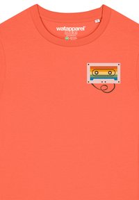 Korallefarbene Baumwoll-T-Shirt mit einem bedruckten Kassettentonband-Graphic in einem Regenbogenfarbschema und einem eingekringelten schwarzen Kassettendraht-Detail.