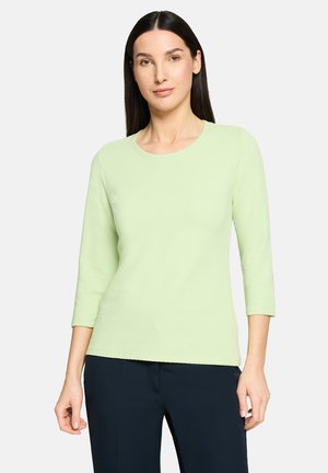 Haut vert clair texturé avec un col rond et des manches trois-quarts, associé à un pantalon bleu foncé. Design simple, sans motifs ni accents.