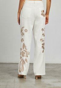 Pantaloni bianchi con intricate ricami floreali beige lungo i lati, con taglio dritto e due tasche posteriori.