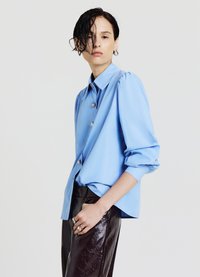 Light blue button-up shirt with puffed sleeves, silver buttons, and a relaxed fit, paired with high-waisted, glossy dark pants.