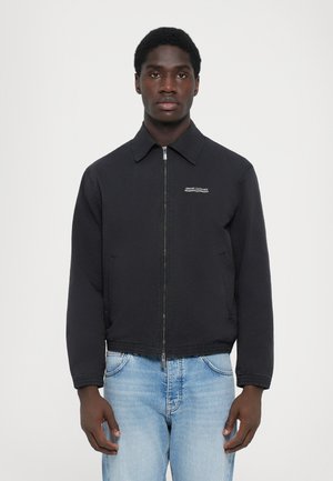 Black bomber jacket with a zip front, collared design, and elastic waist. Features a logo on the chest and is paired with light blue jeans.