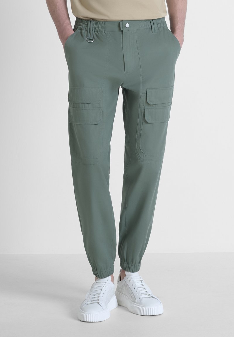 Groene cargobroek met elastische taille, zijzakken, taps toelopende enkels en een lichtgewicht, gladde textuur, gecombineerd met witte sneakers.