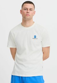 Balta medvilninė marškinėlių su apvalia kaklo iškirpte ir trumpomis rankovėmis. Kairėje krūtinės pusėje yra mėlynas logotipas, o modelis yra laisvo kirpimo.