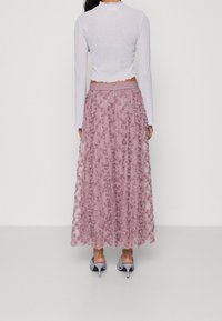 Ljuslila blommig kjol med texturerade rosapplikationer, lagerdesign och bred midja, kombinerad med en vit ribbad långärmad topp.