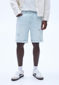 Lyseblå denim shorts med et slidt design, opkrøllede kanter og lommer, parret med hvide sneakers og synlige ankelstrømper.