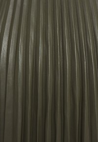 Olivgrön läder med plisserad struktur och vertikala linjer, med en slät yta och subtil lyster. Betonas av rena, enhetliga veck.