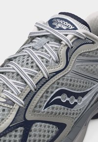 Κοντινό πλάνο στο γκρι και ναυτικό μπλε παπούτσι τρεξίματος Saucony Guide 7 με λευκά κορδόνια και ανώτερο μέρος από ύφασμα πλέγματος.