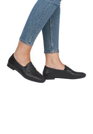 Black leather loafers with a flat sole, featuring horizontal accents across the front, paired with light blue skinny jeans.