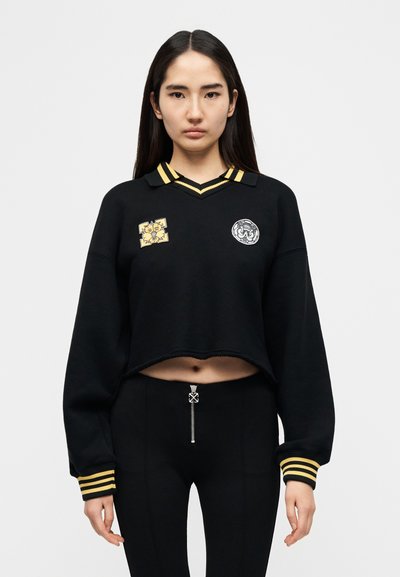 Μαύρο cropped φούτερ με κολάρο ριγέ κίτρινο και μαύρο, με κεντημένα λουλουδένια και κυκλικά μπαλώματα στο στήθος. Μαλακή υφή.