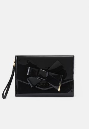 Pochette bracelet noire brillante avec grand détail de nœud et plaque logo Ted Baker dorée sur le rabat avant sur fond blanc.