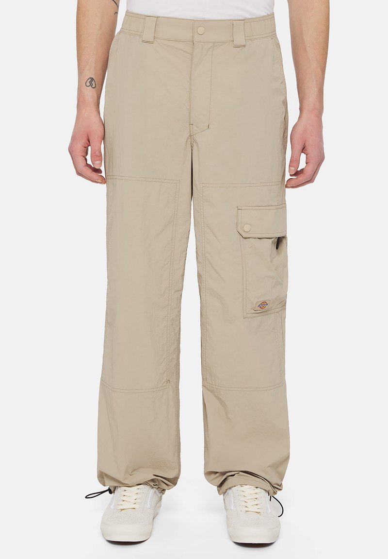 Beige cargo pants made of lightweight fabric, featuring multiple pockets, a relaxed fit, and subtle stitching details. Sneakers are worn with them.