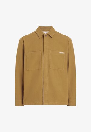 Chaqueta de camisa de algodón marrón con cuello, dos bolsillos frontales y un pequeño parche con logo. Presenta mangas largas y un diseño de corte recto.