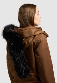 Hnědá prošívaná bunda s černým lemováním kapuce z umělé kožešiny, vybavená zapínáním na zip a logem na rukávu. Hladká textura.