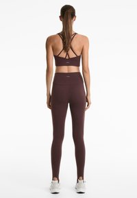 Maroon sports bra with crisscross back design, paired with high-waisted maroon leggings. Both made from stretchy material, featuring a smooth texture.