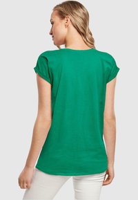 Grünes T-Shirt mit kurzen Ärmeln und umgeschlagenen Bündchen, das eine lockere Passform und eine glatte Baumwolltextur aufweist. Die Rückansicht zeigt einen einfachen, abgerundeten Halsausschnitt.