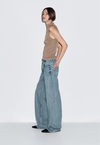 Brown sleeveless top paired with wide-leg light blue jeans. The jeans feature a relaxed fit and subtle stitching details.