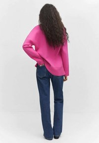 Fuchsia oversized Pullover mit geripptem Muster, kombiniert mit hoch taillierter blauer Jeans mit klassischem Fünf-Taschen-Design und leicht ausgestelltem Bein.