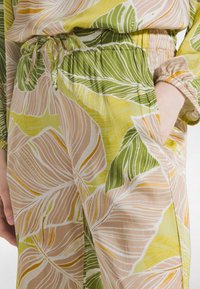 Tela ligera con estampado floral en amarillo, verde y beige. Cuenta con cintura ajustable con cordón y bolsillos laterales con puños elásticos.