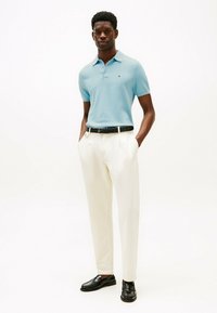 Camiseta polo azul claro, pantalones crema, cinturón negro y mocasines negros. Diseño sencillo con cuello y mangas cortas. El modelo posa con confianza.