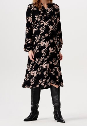 Schwarzes Blusenkleid mit langen Ärmeln, das mit pinken Blumenmustern verziert ist, einem plissierten Ausschnitt und einem midi-langen A-Linien-Schnitt. Kombiniert mit schwarzen kniehohen Stiefeln.
