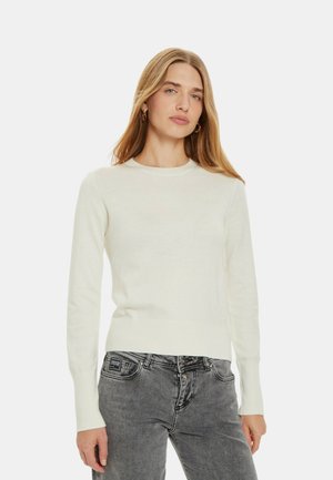 Maglione lavorato a maglia color crema con collo rotondo, polsini e orlo a coste, abbinato a jeans grigi. Design semplice, texture morbida, senza motivi visibili.
