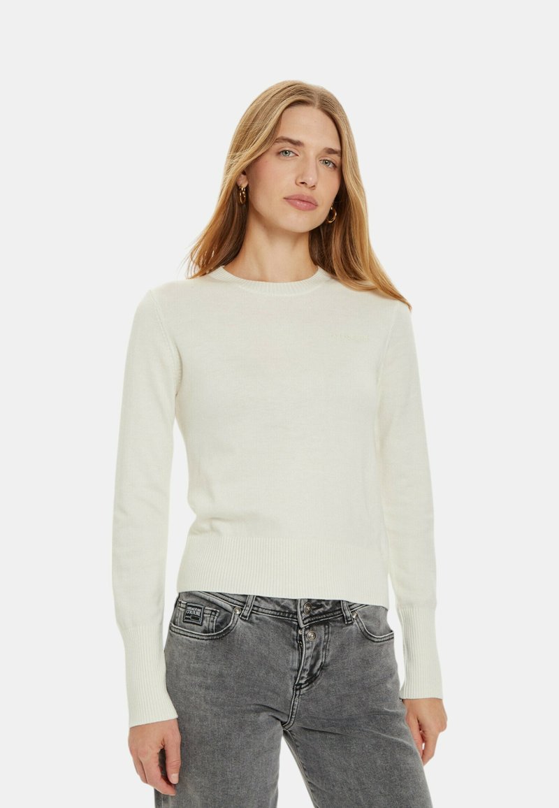 Maglione lavorato a maglia color crema con collo rotondo, polsini e orlo a coste, abbinato a jeans grigi. Design semplice, texture morbida, senza motivi visibili.