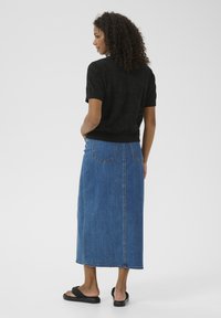 Schwarzes, kurzärmliges, strukturiertes Strickoberteil kombiniert mit einem langen blauen Jeansrock, der über Rückentaschen, sichtbare Nähte und einen geraden Schnitt verfügt.